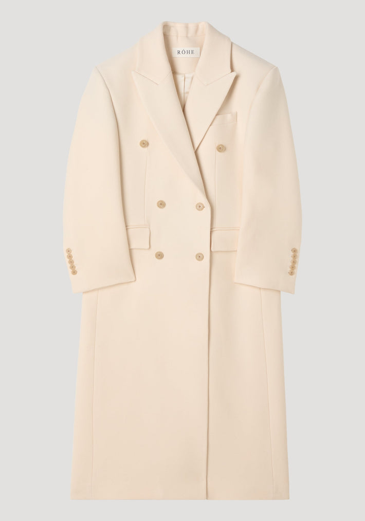 Hourglass wool coat in off white with double-breasted design, peaked lapels, hip flap pockets, and a full-length skirt, showcasing a feminine, structured silhouette.