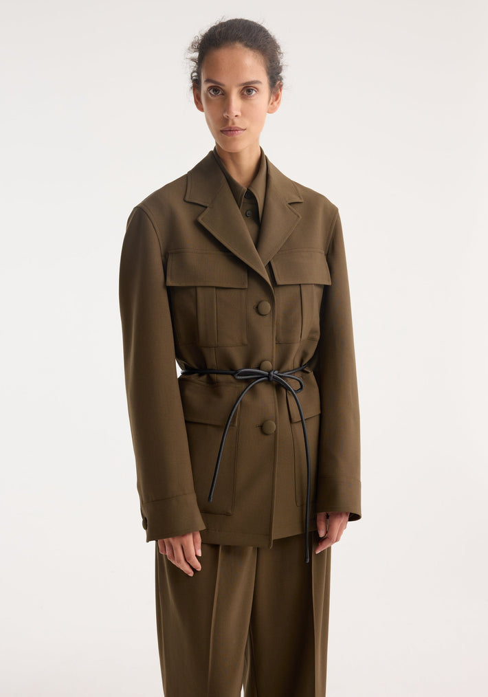 Model wearing Safari blazer-jacket in virgin wool, featuring four flap pockets, cinched with a black leather cord, paired with matching wide-leg trousers.