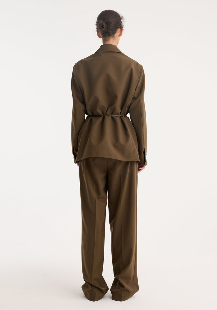 Person wearing a Safari blazer-jacket | forest, featuring a tailored fit with four front patch pockets, cinched waist, and wide-leg trousers, all in virgin wool.