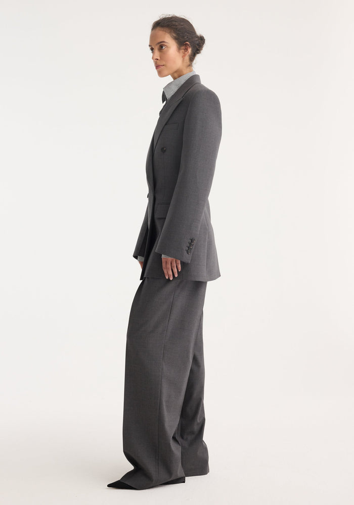 Model wearing Hourglass blazer in dark grey melange, featuring a sharp notch lapel, strong shoulders, and a cinched waist, paired with matching wide-leg trousers.