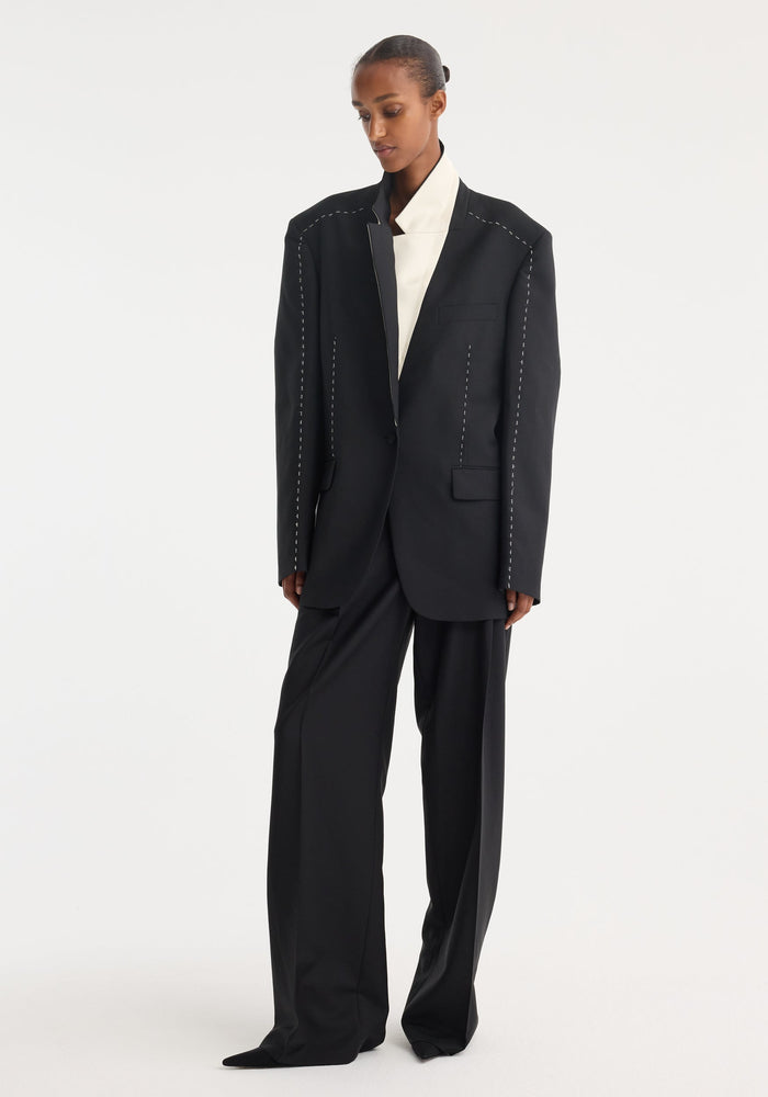 Contrast detail blazer: Oversized black blazer with white basting stitch, single-button closure, high-waisted wide-leg trousers, and high-collared white top. Model's hair in sleek bun.