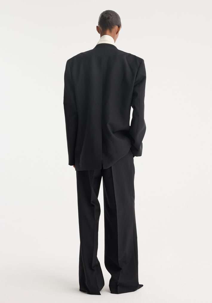 Back view of a model wearing an oversized Contrast Detail Blazer with contrast stitching, revealing a crisp white shirt collar and wide-leg trousers.