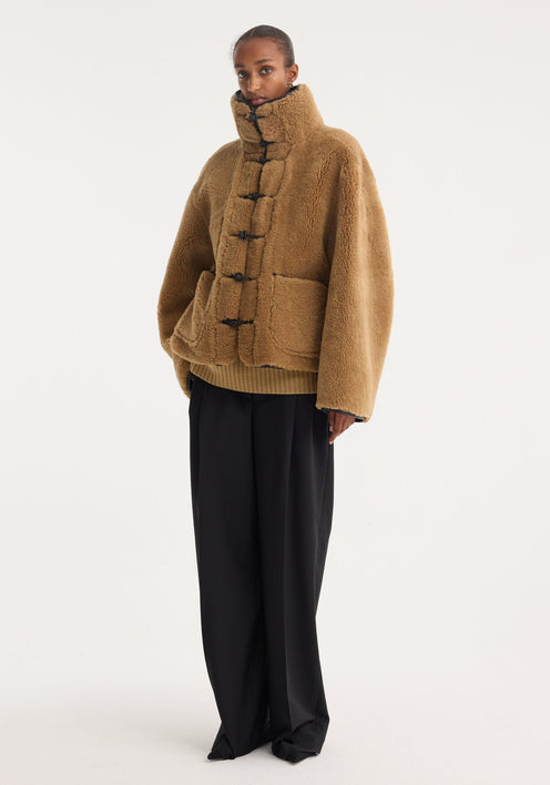 Shearling coat | cognac features a plush, camel brown texture, mandarin closures, stand-up collar, patch pockets, and leather trim, offering a cozy, oversized style.