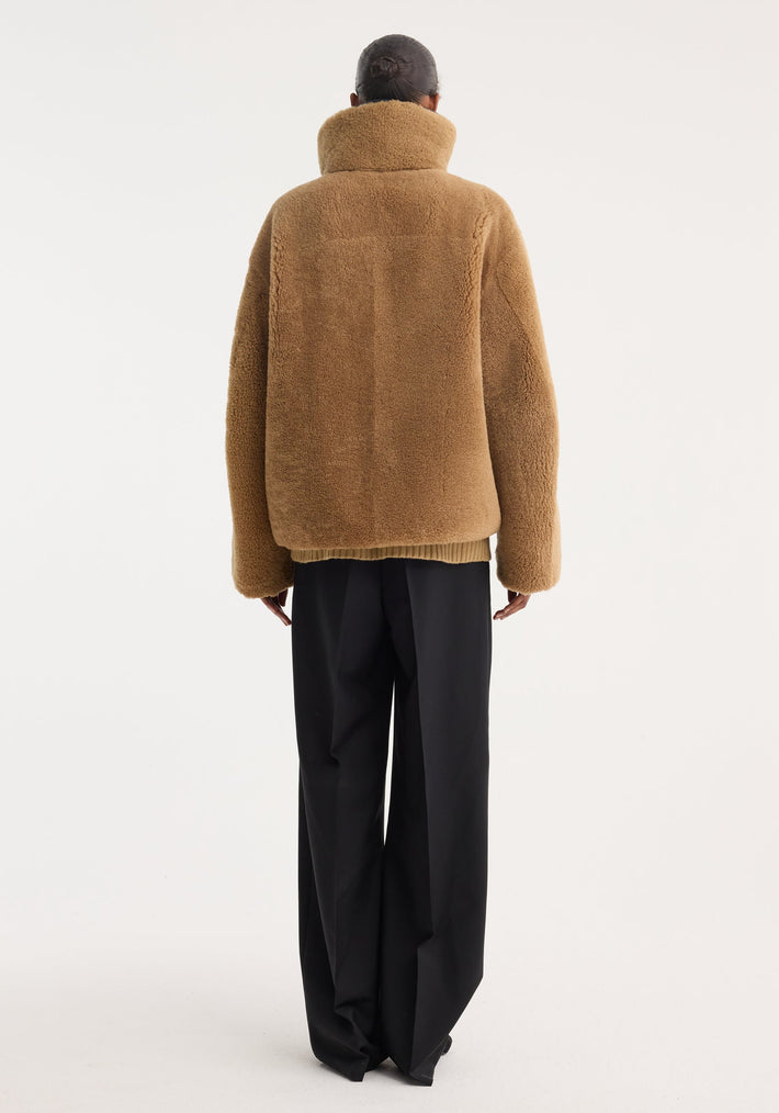 Shearling coat | cognac shown from the back, featuring a stand-up collar, mandarin closures, leather trim, and patch pockets, paired with wide-leg trousers.