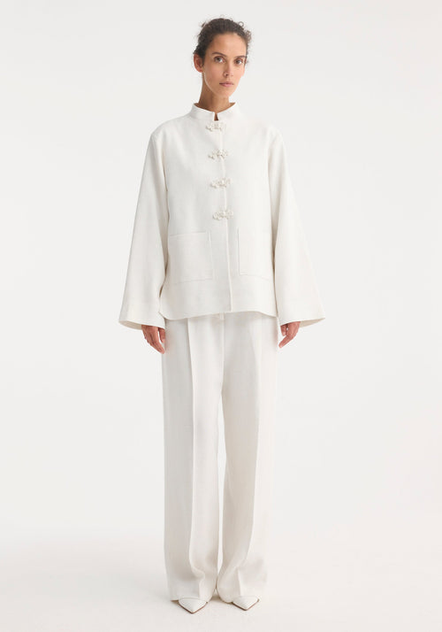 Person wearing a minimalist Mandarin jacket 'Marie' in winter white, featuring wide sleeves, pankou closures, and patch pockets, paired with matching wide-leg trousers.