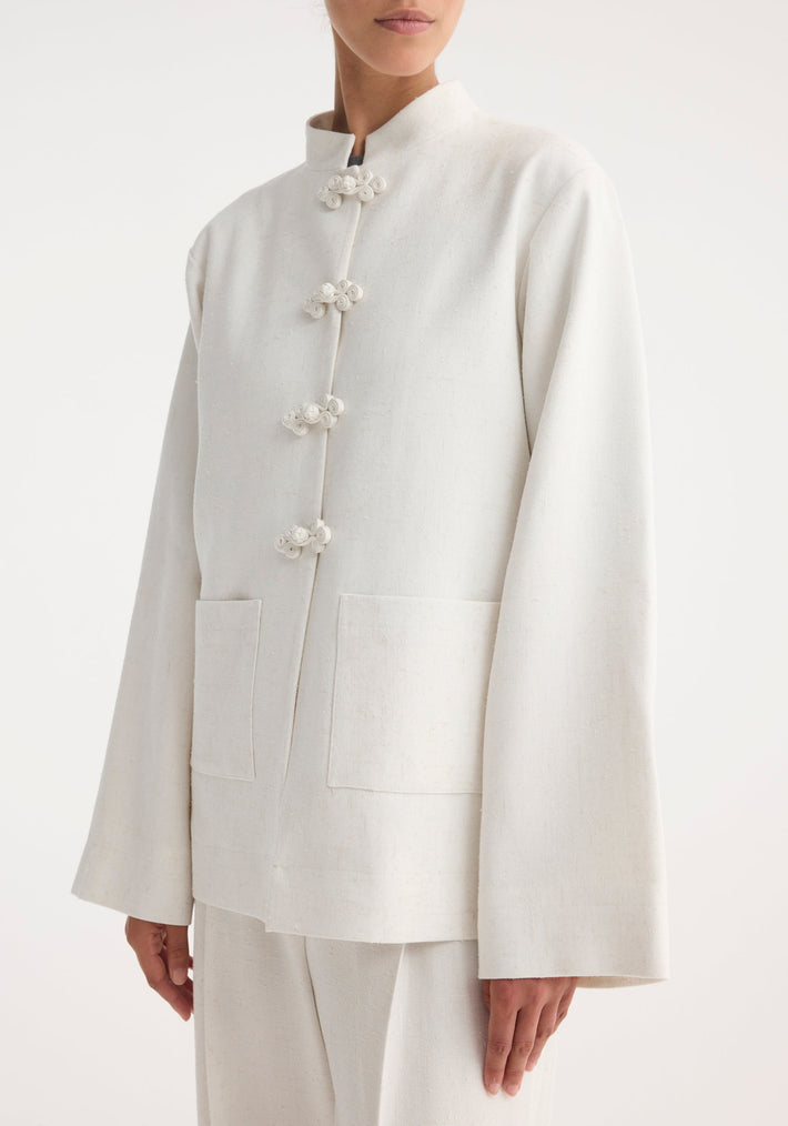 Mandarin jacket in winter white, featuring a modern collarless design, pankou closures, patch pockets, and wide, flared sleeves. Paired with loose-cut trousers.