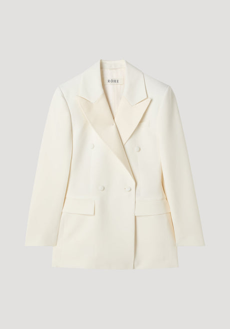 Hourglass tuxedo blazer in off white, featuring a double-breasted design, peaked lapels, and flap pockets, highlighting a structured silhouette with a cinched waist and strong shoulders.