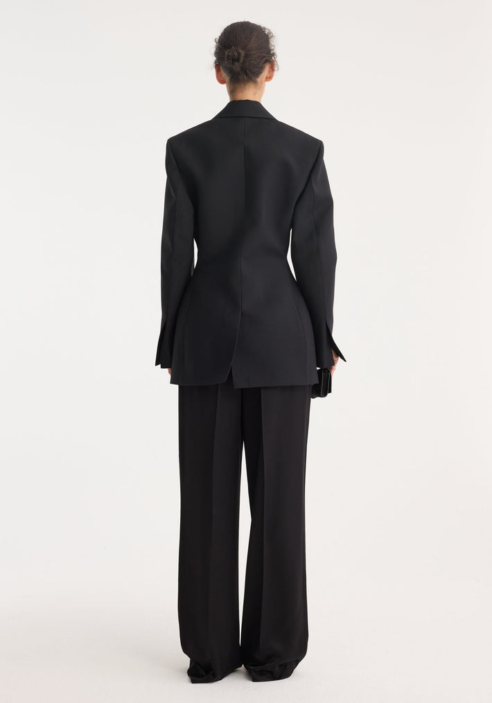 Hourglass tuxedo blazer in black, featuring a structured silhouette with notch lapel, wide-leg trousers, and model holding a small clutch.