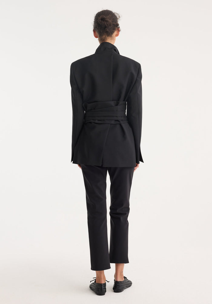 Kimono belted blazer in black with a wrap sash belt, tailored from a wool mohair blend, worn by a model with trousers and slip-on shoes.