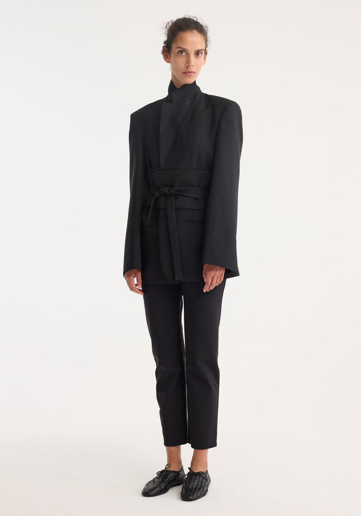 Model wearing Kimono belted blazer in black with wide kimono sleeves, wrap sash belt, and slim-cut trousers, showcasing a modern, structured look.