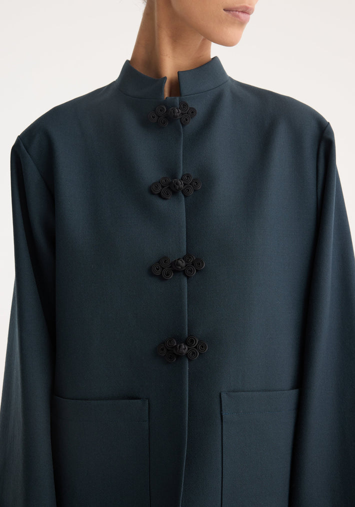Mandarin jacket | storm: Dark teal mandarin-collar coat with black pankou closures, patch pockets, and wide sleeves, worn by a partially visible model. Crafted from 100% virgin wool.