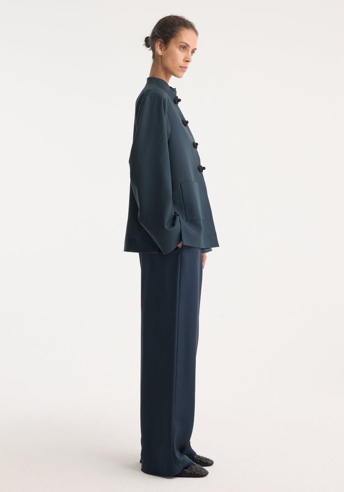 Woman in a Mandarin jacket | storm, featuring wide sleeves, pankou closures, patch pockets, paired with matching wide-leg trousers and dark woven slip-on shoes.