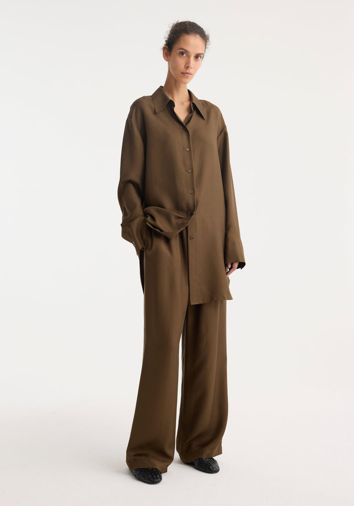 Signature elongated silk shirt | forest, oversized fit with statement collar and cuffs, worn with matching wide-leg trousers, offering a minimalist and androgynous look.