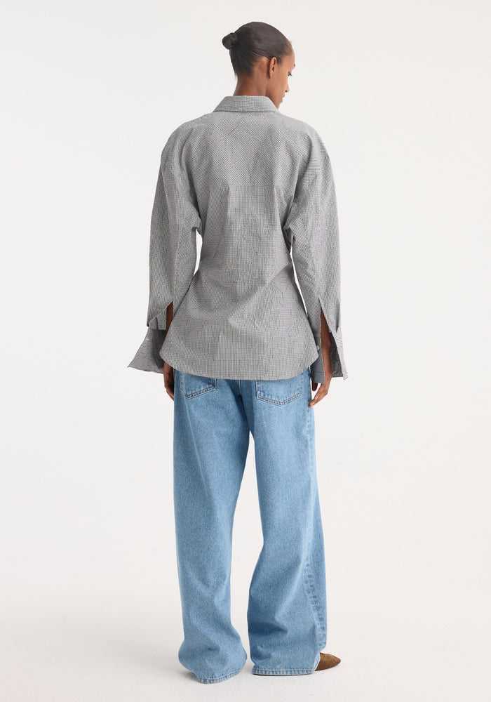 Crushed checked shaped shirt in mini grey check, with a soft sculpted silhouette, worn with light-blue denim jeans, seen from behind, studio shot.
