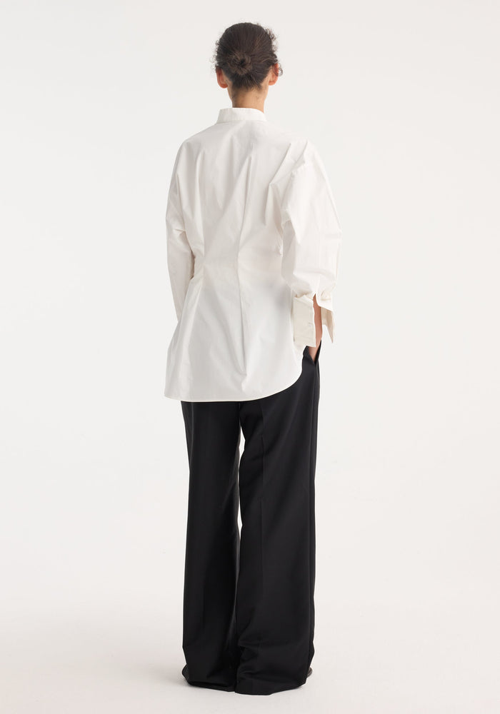 Person wearing the Tuxedo Wired Shaped Shirt with drop shoulders, stand collar, and statement cuffs, paired with wide-leg trousers, viewed from the back.