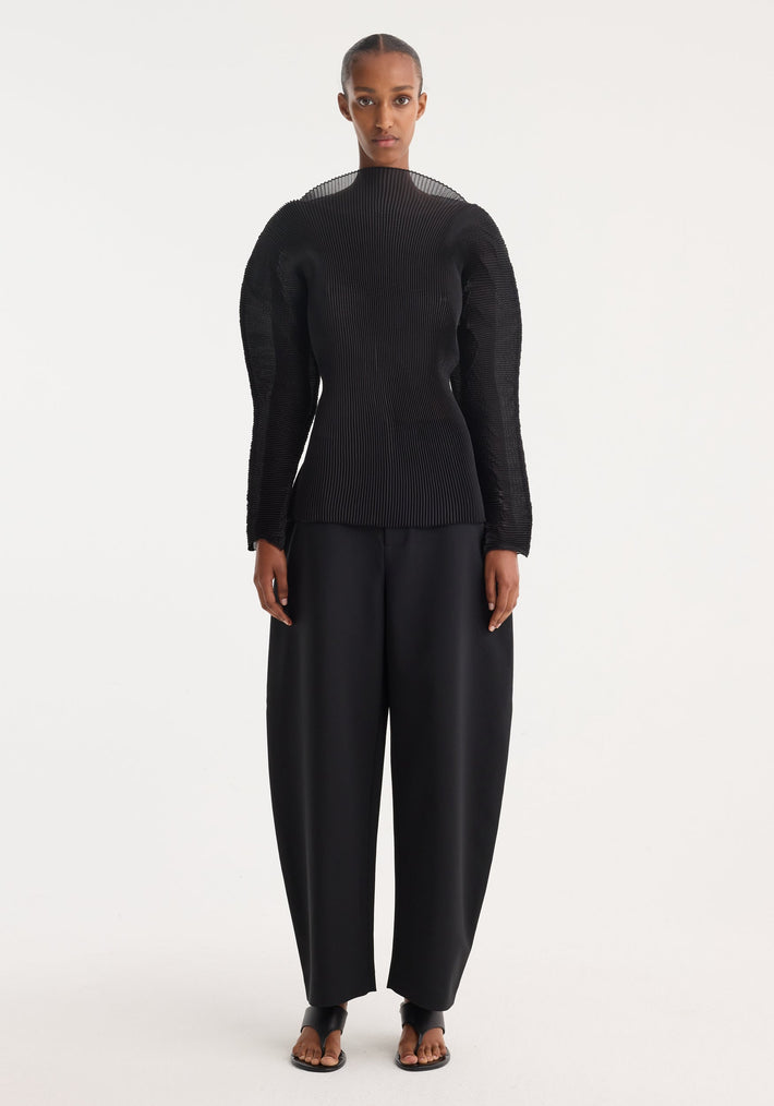 Woman wearing Sculptural plissé top in black, featuring voluminous sleeves and a high neckline, paired with wide-leg trousers and minimalist sandals.