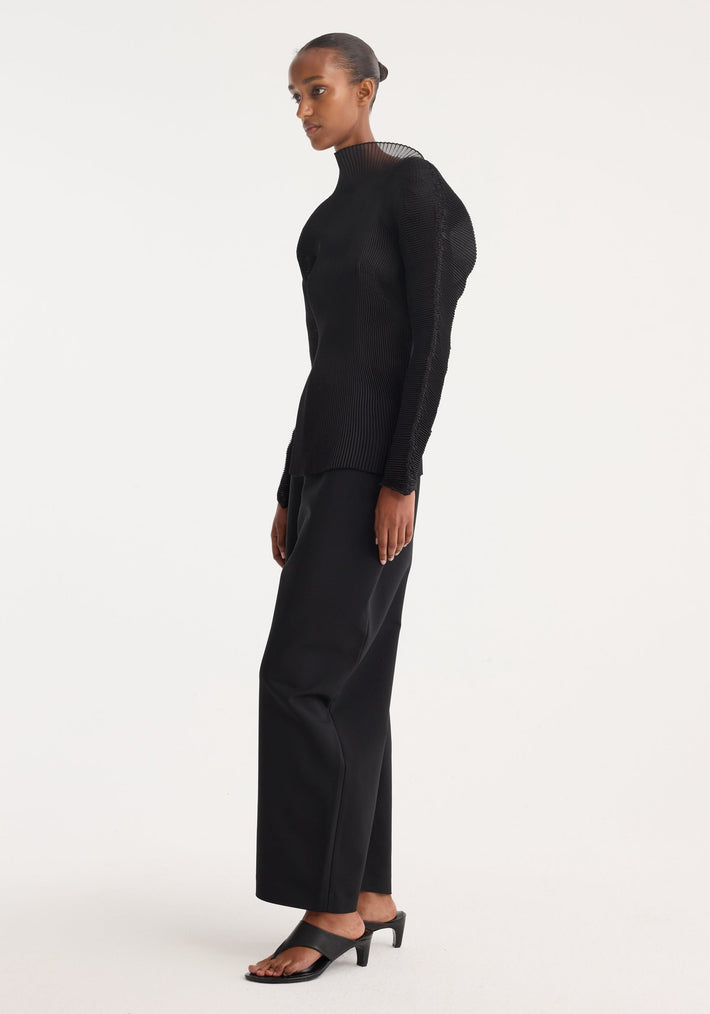 Model wearing Sculptural plissé top | black: high-neck, semi-transparent, sculptural silhouette with voluminous sleeves, paired with wide-leg trousers and open-toe heeled sandals.