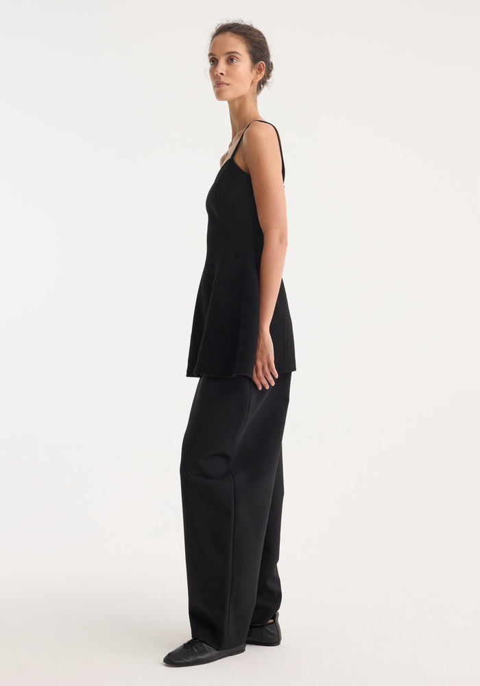 Woman in profile wearing a Bustier double-faced top with peplum waist and thin straps, paired with wide-leg trousers, showcasing a sophisticated silhouette.