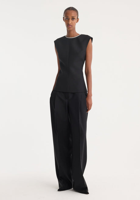 Model in sleeveless, form-fitting Open back appliqué top | black, showcasing crystal detailing on open back, paired with high-waisted, wide-leg trousers against a plain background.