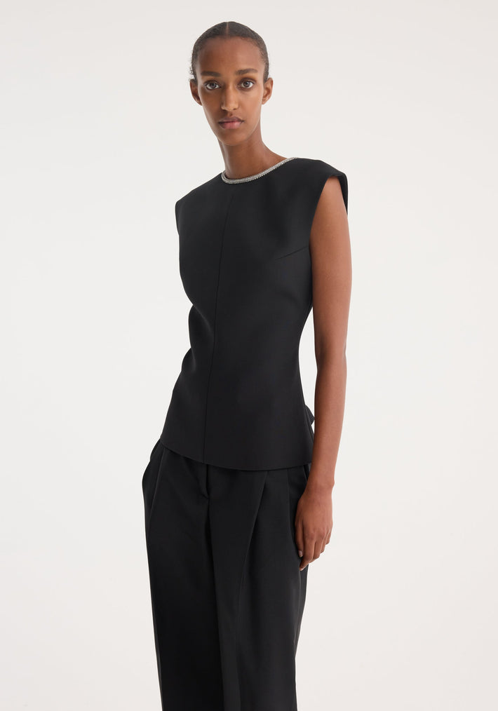 Model wearing the Open back appliqué top in black, showcasing its sleeveless design, subtle shoulder padding, and crystal embellishments on a tailored silhouette.
