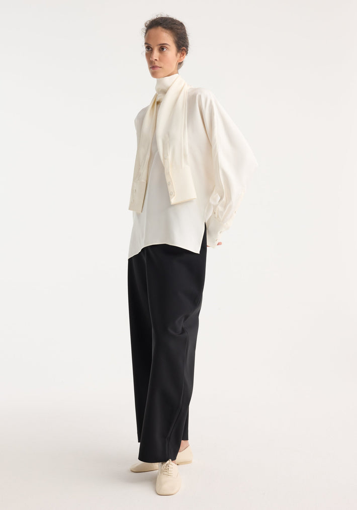 Model wearing Foulard silk top with draped sleeves, layered over a high-neck top, paired with loose black trousers and cream lace-up flats.