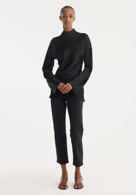 Model wearing a Satin waisted top | black, featuring a mock neck, long flared sleeves, and a slim-fit design with a seamless back zip closure.