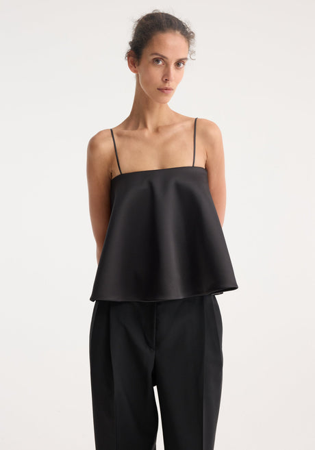 Peplum satin top with adjustable straps and straight neckline, worn by a model with high-waisted trousers, showcasing its elegant, fitted silhouette.