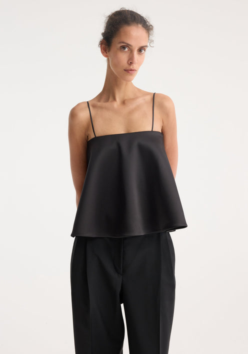 Peplum satin top with adjustable straps and straight neckline, worn by a model with high-waisted trousers, showcasing its elegant, fitted silhouette.