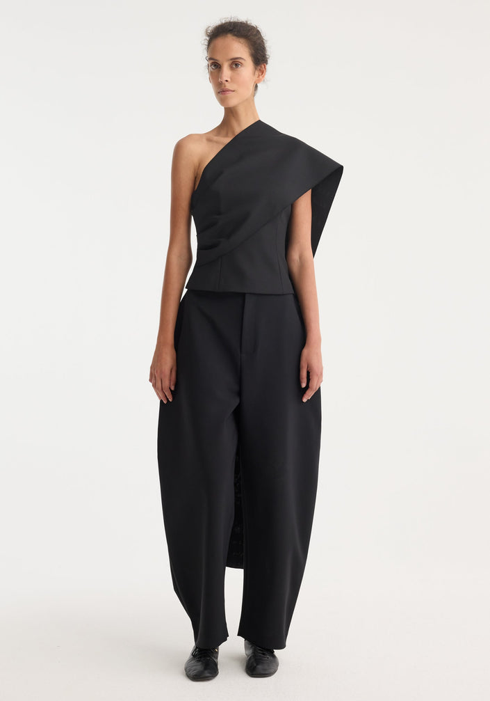 Black, high-waisted trousers with asymmetric draped sash detail at waist, showcasing one leg. Part of the One-shoulder cape top | black collection.