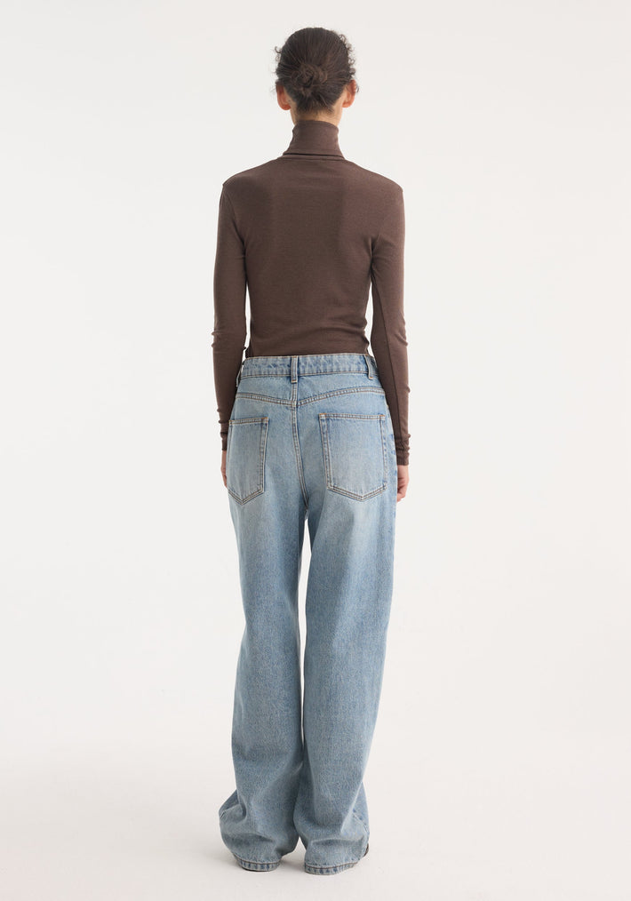 Person wearing Fine merino turtleneck in brown melange, fitted with long sleeves, paired with high-waisted, wide-leg light-wash jeans, hair in a bun.