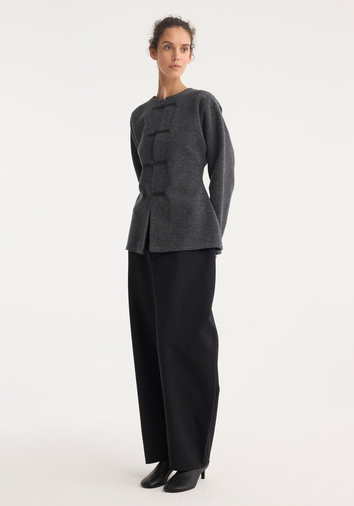 Mandarin waisted cardigan in mid grey melange with leather pankou closures, round neckline, long sleeves; paired with wide-leg black trousers and ankle boots.