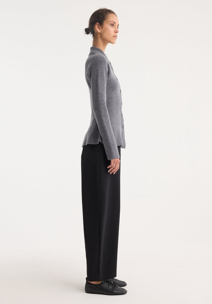 Side-profile of a person wearing the Waisted rib cardigan in dark grey melange, featuring a fitted silhouette with peplum flare and button-front detail.