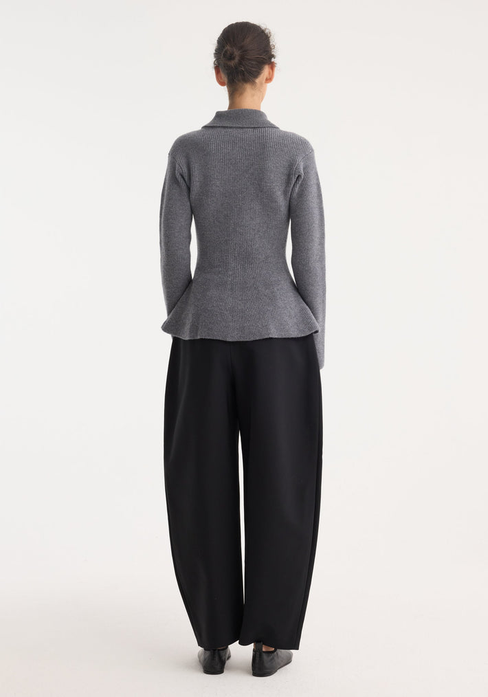 Rear view of person in a waisted rib cardigan with peplum flare, polo collar, and button-down front, paired with wide-leg trousers and slip-on shoes.