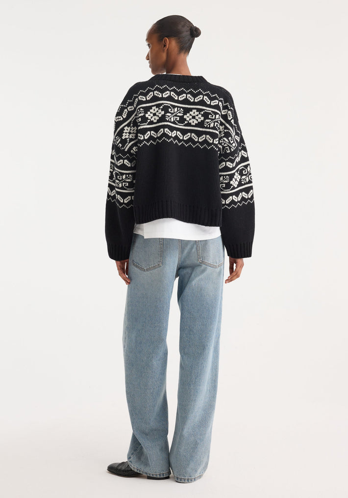 Woman wearing Fair-isle knitted jumper | black, featuring a classic pattern, boxy fit, slightly cropped. Paired with light-wash wide-leg jeans and slip-on shoes.