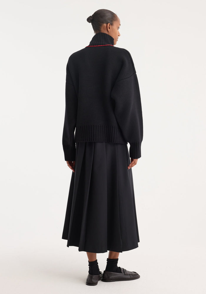 Model in a Sculptural compact turtleneck | black, showcasing its chunky knit, relaxed fit, and dropped shoulders, paired with a mid-calf A-line skirt.