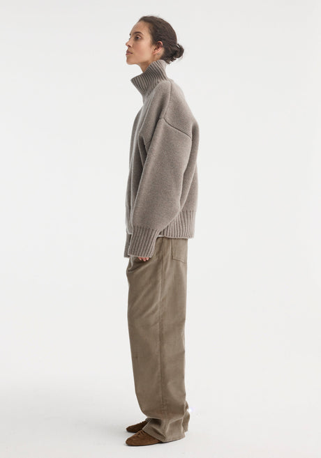 Woman wearing Sculptural compact turtleneck | clay melange, an oversized grey knit with drop shoulders, over loose taupe trousers, styled with brown suede lace-up shoes.