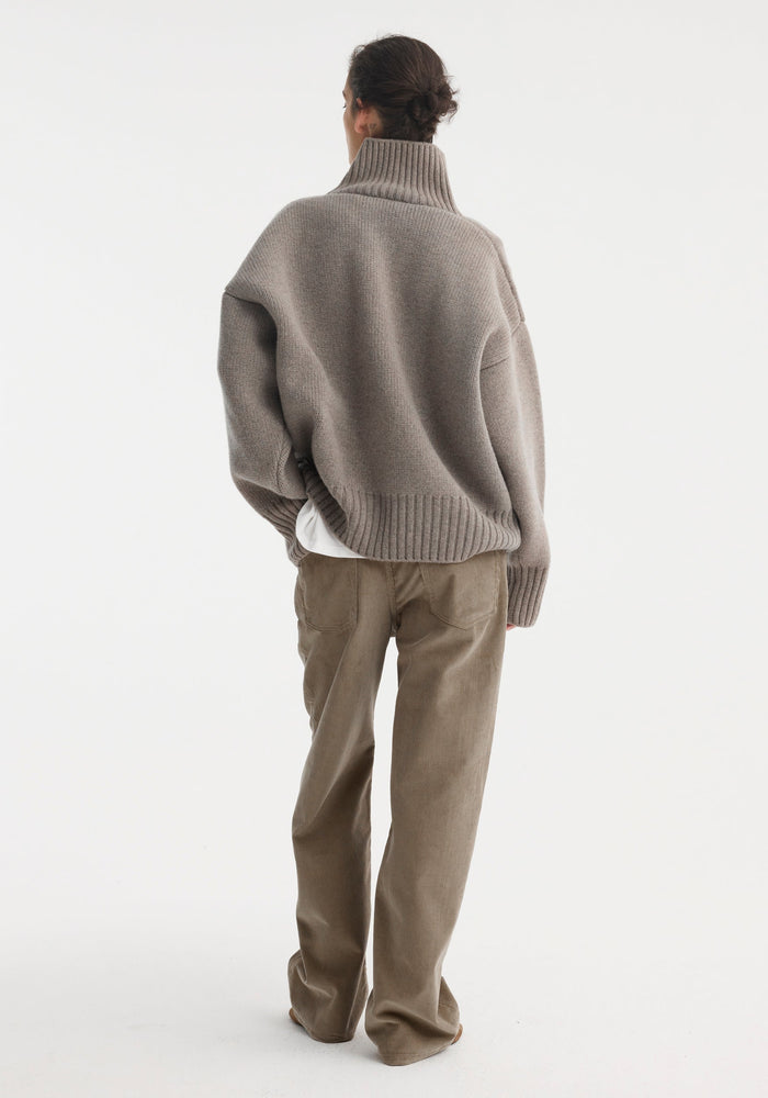 Person wearing a Sculptural compact turtleneck in clay melange, showcasing its relaxed fit and drop shoulder, paired with wide-leg corduroy trousers.