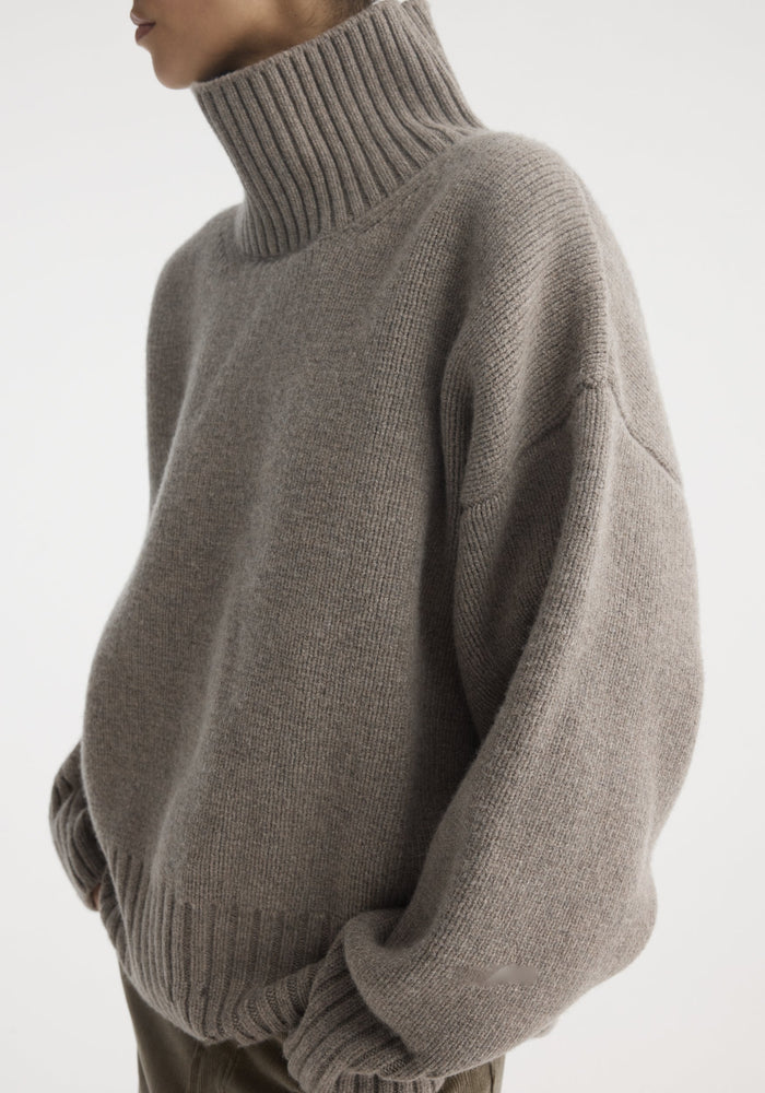 Sculptural compact turtleneck in clay melange, showcasing a high-neck, ribbed cuffs, and hem. Worn over corduroy trousers, highlighting its relaxed fit and volume.
