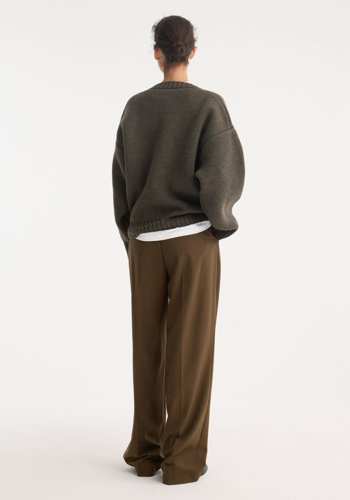 Sculptural compact v-neck knit in forest melange, layered over a white tee, paired with high-waisted, wide-leg trousers, showcasing a relaxed, stylish fit.