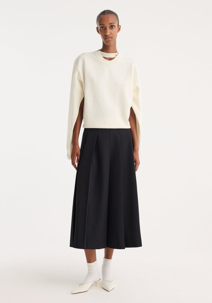 Model in minimalist attire showcasing a Crewneck with open neck | off white, featuring draped sleeves and a key-hole detail, paired with a black midi skirt.