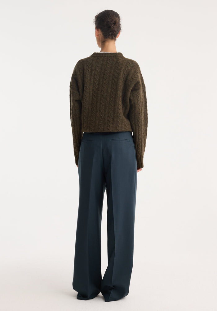 Person wearing Mid-waist tailored trousers, featuring a high-waisted, wide-leg fit, and double pleats, crafted from soft virgin wool, viewed from the back.