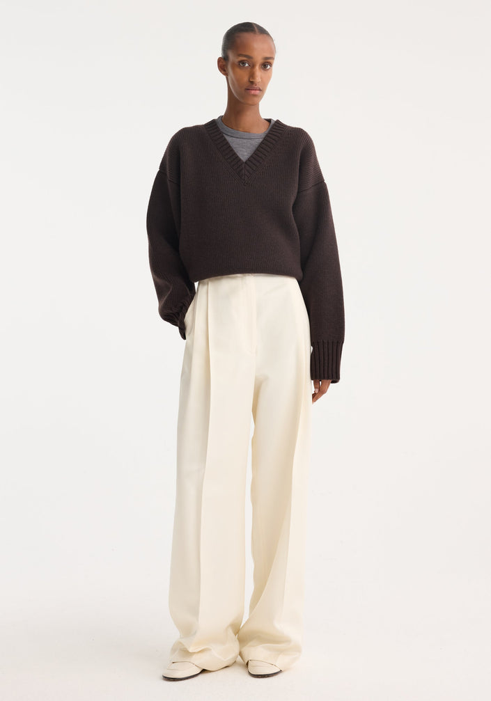 High-waist satin trousers in cream with a tailored waistband, front and back pleats, and welt pockets, laid flat on a neutral background.