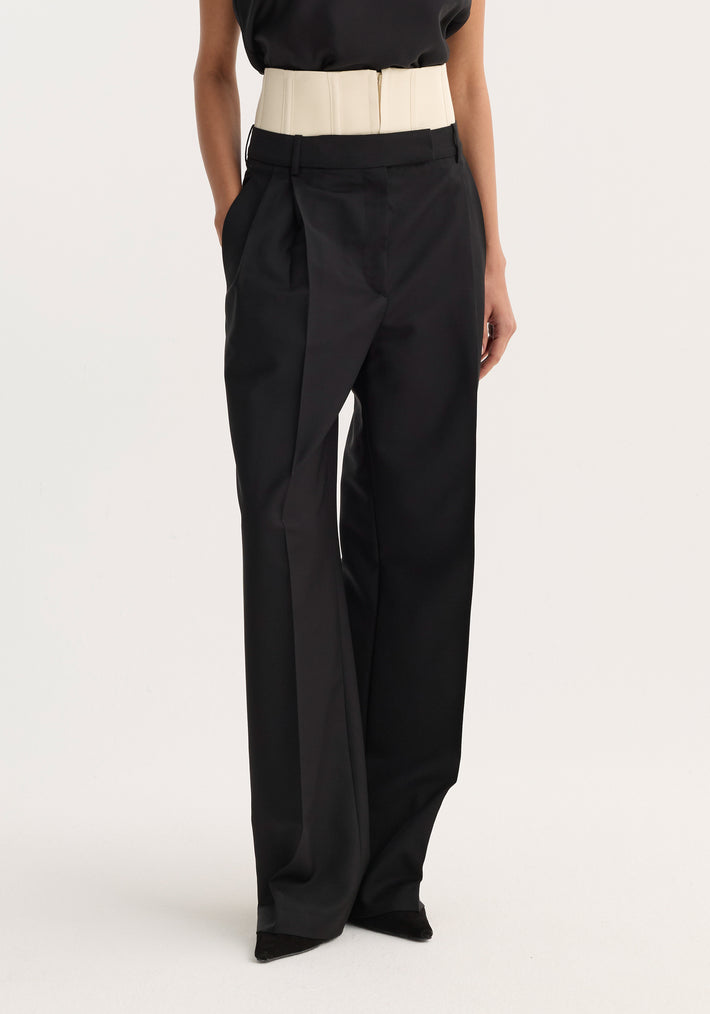 Model wearing black Corset Trousers with a cream corset waist belt, high-waisted and tailored, over loose-fitting trousers and pointed shoes, showcasing elegant structure.