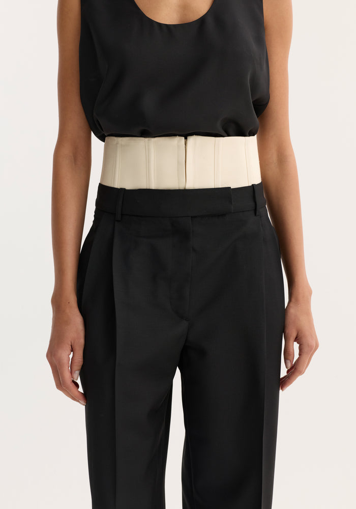 Model wearing Corset trousers | black, featuring a structured cream waist corset over a sleeveless black top and high-waisted tailored black trousers.