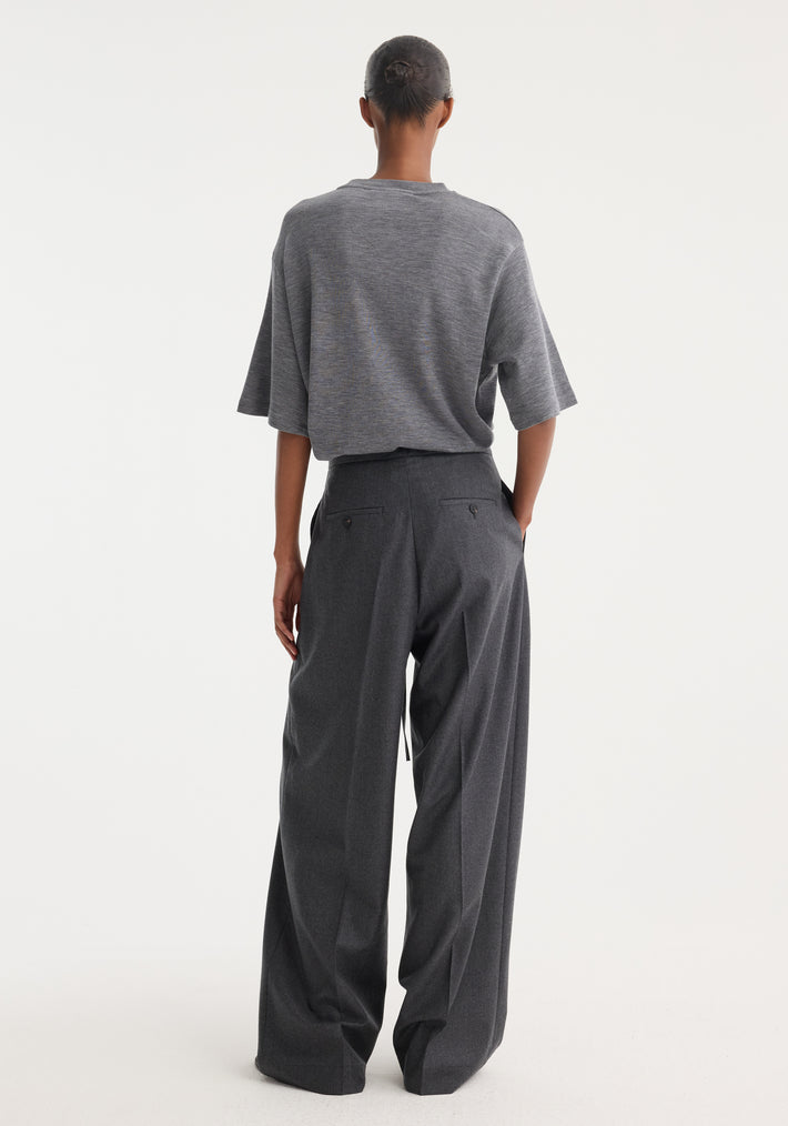 Person wearing Relaxed soft wool trousers | dark grey melange, featuring a wide-leg silhouette and drawstring waistband, crafted from lightweight virgin wool. Hair styled in a neat bun.