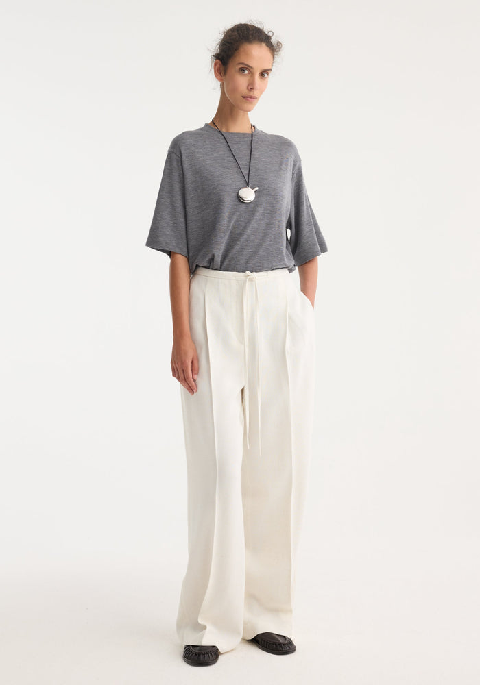 Model wears Relaxed drawstring trousers in winter white, showcasing a wide-leg, high-waisted design with a comfortable drawstring waistband, paired with a grey T-shirt.