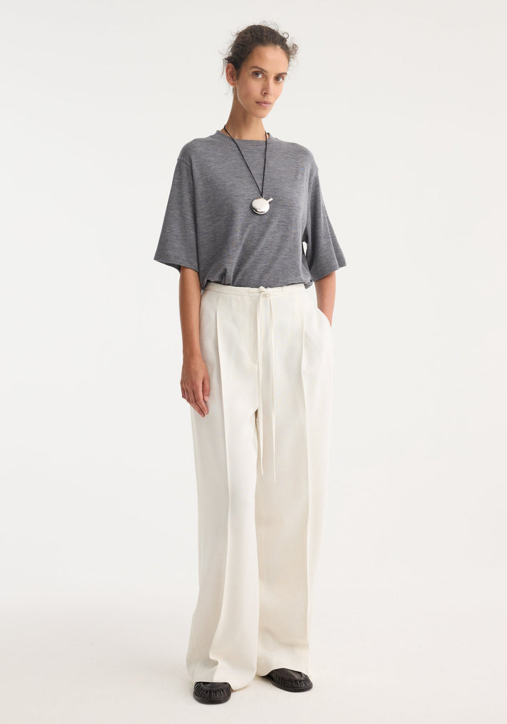 Model wears Relaxed drawstring trousers in winter white, showcasing a wide-leg, high-waisted design with a comfortable drawstring waistband, paired with a grey T-shirt.