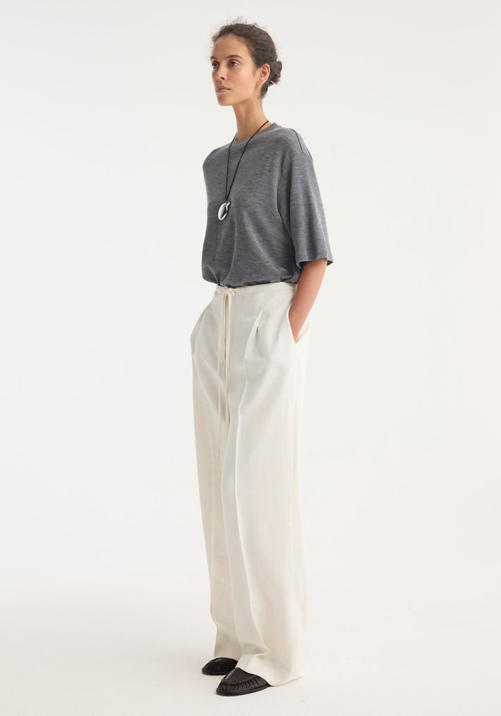 Model wearing Relaxed drawstring trousers in winter white, showcasing a wide-leg fit and drawstring waistband, paired with a grey T-shirt and dark loafers.
