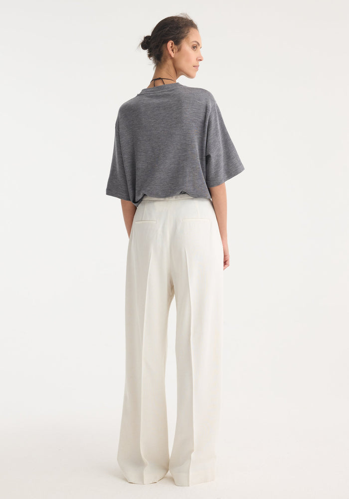Person wears relaxed drawstring trousers in winter white, featuring a wide-leg silhouette and elegant waistband, styled with a tucked gray top for effortless movement.