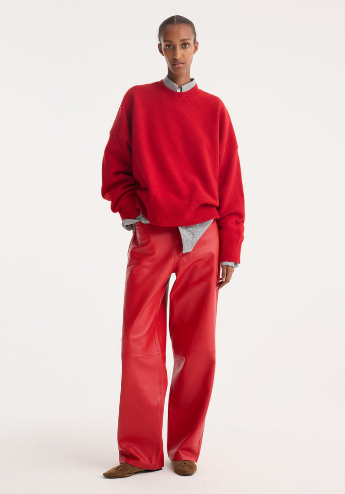 Model wearing Baggy Leather Trousers | Rosso, featuring a high-waist, wide-leg fit in soft nappa lamb leather, paired with a red sweater and loafers.